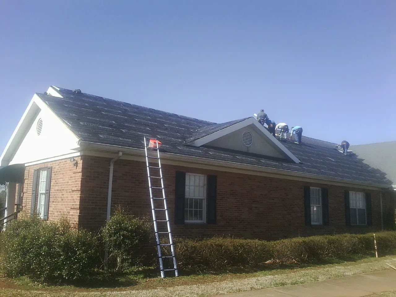 Crew tearing shingles off a brick ranch roof with a ladder set — Emergency Roof Repair work by our crew in Sparks