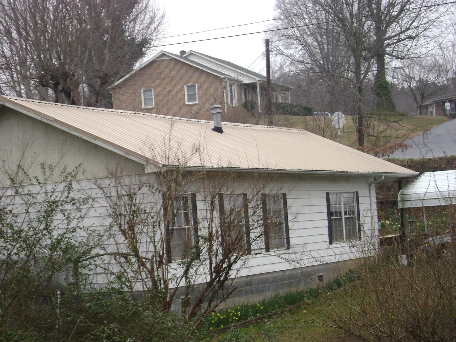 Tan metal roof on a white sided house set into a hillside — Commercial Roofing by Roofing Brothers in Sparks